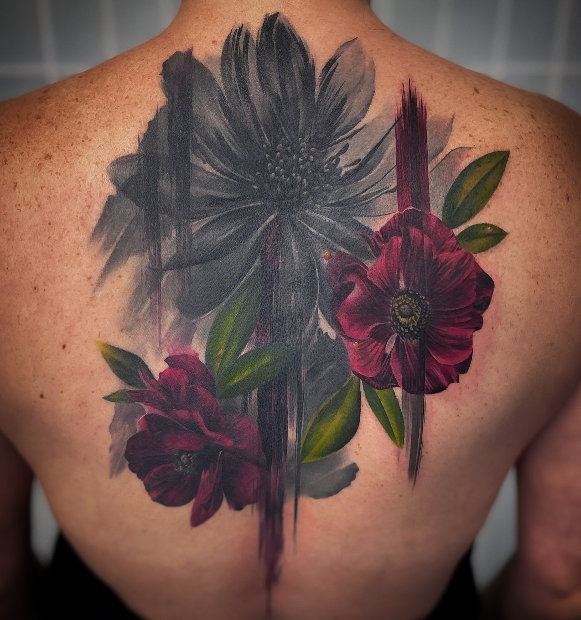 Floral back tattoo with painterly black and colour detail