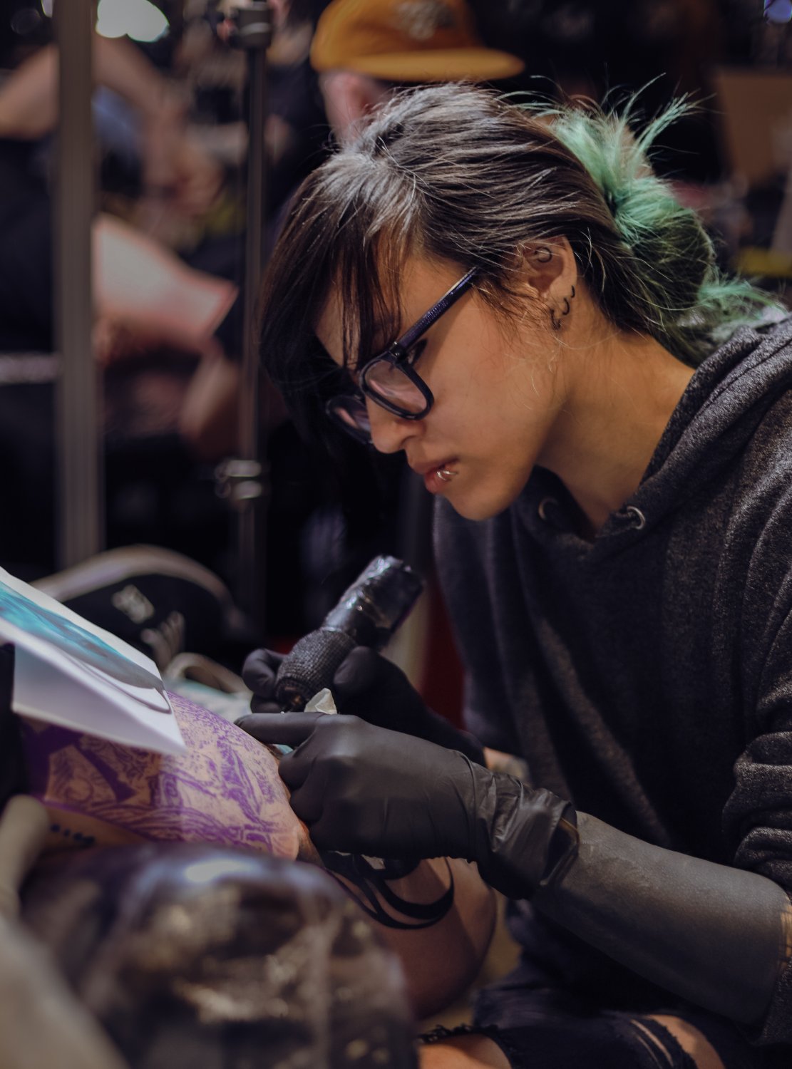 Kimmi Gayle tattooing at a convention with green hair